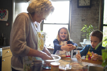 Happy children with grandmother mixing flour in kitchen - CAVF40470