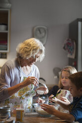 Frau gibt Zucker in den Teig, während sie mit Kindern in der Küche Kekse backt - CAVF40477