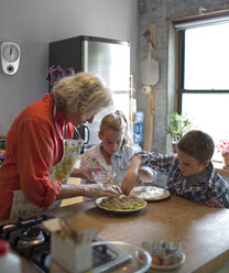 Kinder mit Großmutter, die in der Küche das Essen garnieren - CAVF40487