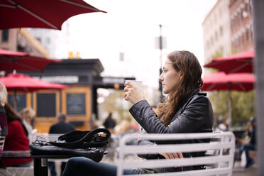 Nachdenkliche Frau hält Kaffeetasse, während sie in einem Straßencafé in der Stadt sitzt - CAVF40559