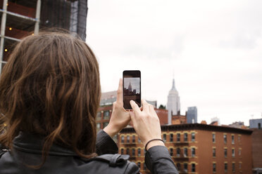 Rear view of woman photographing Empire State Building through smart phone in city - CAVF40571