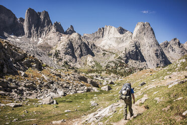 Rear view of hiker walking on field by rock formations - CAVF40573