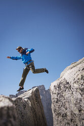 Wanderer springt auf Felsformationen vor blauem Himmel - CAVF40586