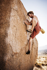 Seitenansicht eines Mannes ohne Hemd, der an einem sonnigen Tag auf einen Felsen klettert - CAVF40601
