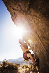 Mann ohne Hemd klettert an einem sonnigen Tag gegen den klaren Himmel auf einen Felsen - CAVF40603