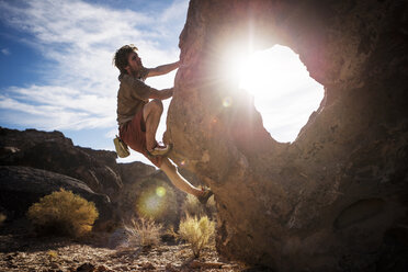 Mann klettert Felsen gegen den Himmel an einem sonnigen Tag - CAVF40610