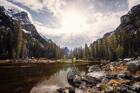 Mann steht auf einem Felsen in einem See im Grand Teton National Park vor dem Himmel, lizenzfreies Stockfoto