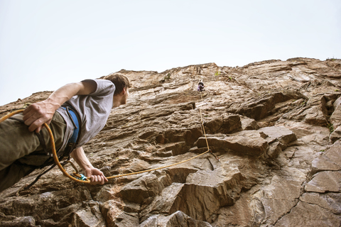 Niedriger Blickwinkel eines Mannes, der einen Freund beim Bergsteigen beobachtet, lizenzfreies Stockfoto