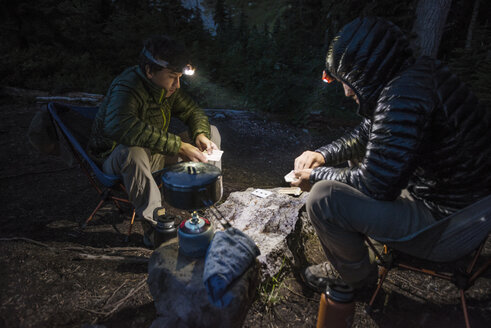 Freunde spielen Kartenspiel beim Camping im Wald in der Abenddämmerung - CAVF40682