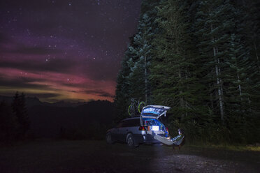 Wanderer schaut auf Laptop, während er im Wald bei einem Auto vor einem Sternenfeld rastet - CAVF40688
