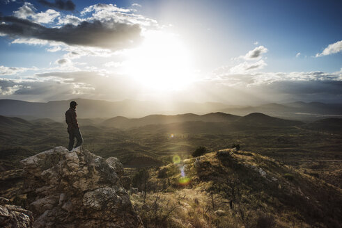 Wanderer steht auf einem Felsen in den Bergen gegen den Himmel an einem sonnigen Tag - CAVF40696