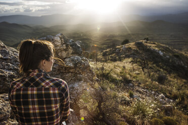 Wanderer sitzt auf einem Felsen und schaut auf die Berge an einem sonnigen Tag - CAVF40697