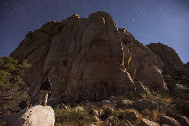 Niedriger Blickwinkel auf einen Wanderer, der auf einem Felsen steht und auf einen Berg mit Sternenhimmel blickt - CAVF40704