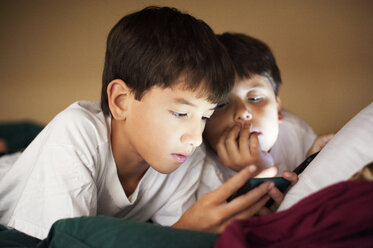 Brothers looking in phone while resting on bed at home - CAVF40721