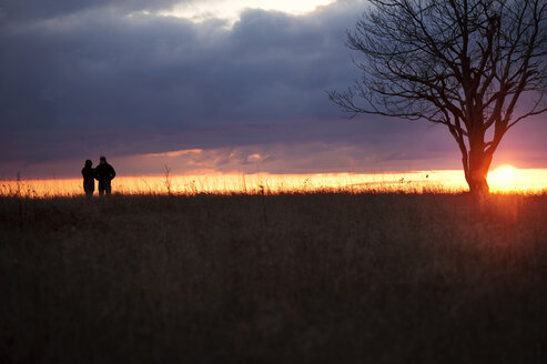 Silhouette Paar stehen auf grasbewachsenen Feld gegen dramatischen Himmel - CAVF40726