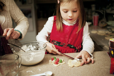 Schwester, die einem Mädchen beim Verzieren von Keksen am Küchentisch hilft - CAVF40731