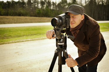 Photographer with tripod on road against forest - CAVF40732