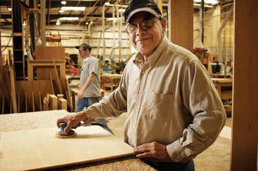 Porträt eines lächelnden Mannes, der in einer Werkstatt Holzbretter abschleift - CAVF40751