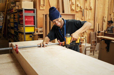 Glücklicher Schreiner beim Bohren von Holzbrettern in der Werkstatt - CAVF40756