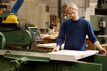 Seriöser Schreiner bei der Arbeit mit Maschinen an einem Holzbrett in der Werkstatt - CAVF40764