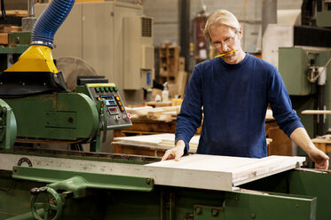 Serious carpenter using machinery on wooden plank at workshop - CAVF40764