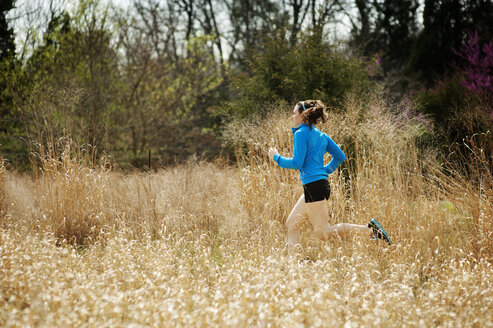 Sportlerin läuft inmitten eines Feldes gegen Bäume - CAVF40768