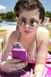 Woman wearing sunglasses using phone while lying at beach on sunny day - CAVF40775