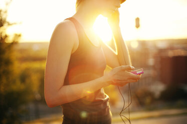 Mittelteil eines Sportlers, der beim Training an einem sonnigen Tag Musik über sein Handy hört - CAVF40779