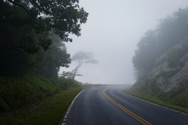 Empty road amidst mountains against sky during foggy weather - CAVF40792