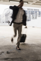 Businessman with rolling suitcase in a hurry at parking garage - UUF13424