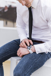Geschäftsmann sitzt im Freien und benutzt eine Smartwatch - UUF13428