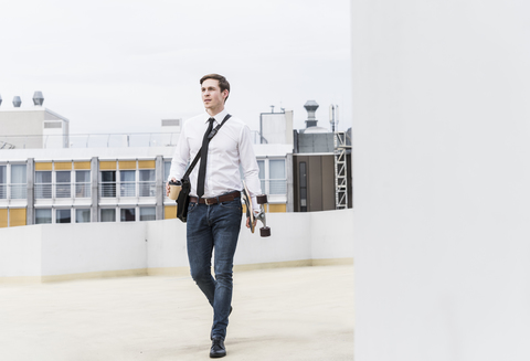 Geschäftsmann mit Kaffee zum Mitnehmen und Skateboard in einem Parkhaus, lizenzfreies Stockfoto