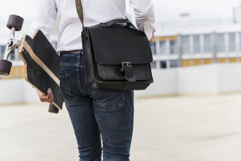 Businessman with and skateboard walking at parking garage - UUF13430