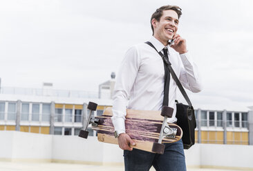 Glücklicher Geschäftsmann mit Handy und Skateboard in einem Parkhaus - UUF13431