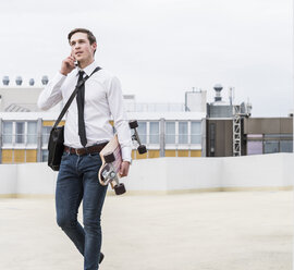 Businessman with cell phone and skateboard walking at parking garage - UUF13432