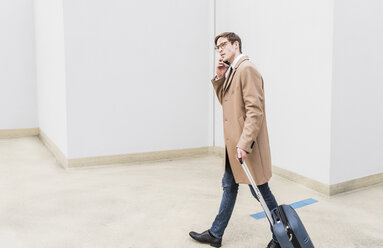Businessman with rolling suitcase on the phone at parking garage - UUF13441