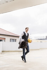 Smiling businessman with basketball walking at parking garage - UUF13448