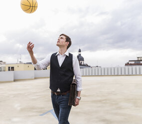 Businessman throwing up basketball at parking garage - UUF13450