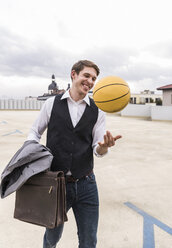 Happy businessman with basketball walking at parking garage - UUF13451