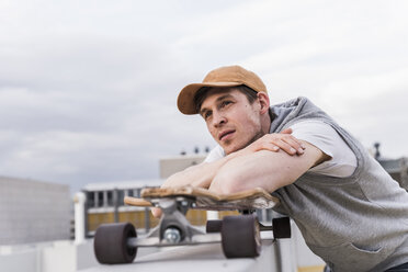 Mann mit Skateboard lehnt an einer Wand und schaut sich um - UUF13458