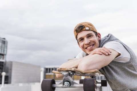 Porträt eines lächelnden Mannes mit Skateboard, der sich an eine Wand lehnt, lizenzfreies Stockfoto