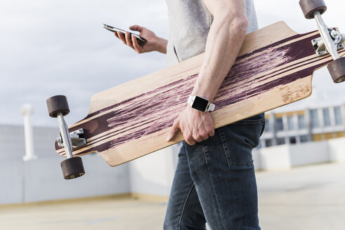Nahaufnahme eines Mannes mit Mobiltelefon und Skateboard in einem Parkhaus - UUF13460