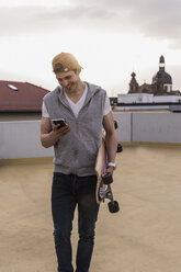 Smiling man with cell phone and skateboard walking at parking garage - UUF13461