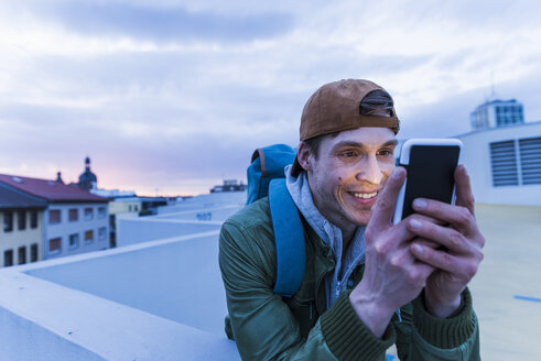 Lächelnder Mann, der in der Abenddämmerung auf ein glänzendes Smartphone schaut - UUF13464