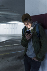 Smiling man looking at shining smartphone in parking garage - UUF13465