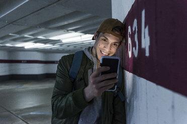 Lächelnder Mann schaut auf ein glänzendes Smartphone in einem Parkhaus - UUF13466