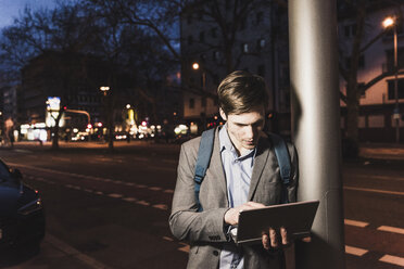 Businessman using laptop on urban street at night - UUF13471