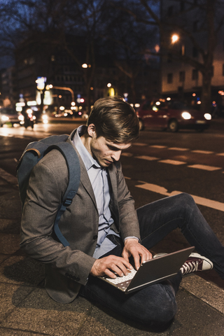 Geschäftsmann mit Laptop auf einer nächtlichen Straße in der Stadt, lizenzfreies Stockfoto