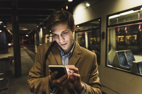 Geschäftsmann mit Handy an der Straßenbahnhaltestelle bei Nacht, lizenzfreies Stockfoto