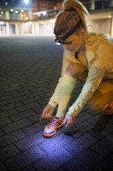 Female athlete tying shoelace on footpath at night - CAVF40805